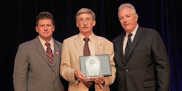 Eric Frost holding award standing between two men.