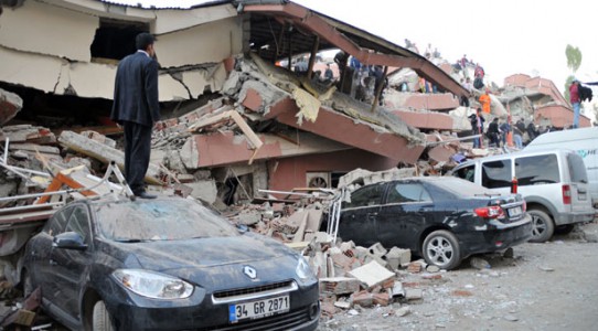 Man standing on top of car, collapsed building in Van, Turkey.