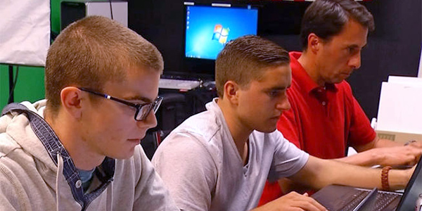 three male students sitting at desk with laptop computers