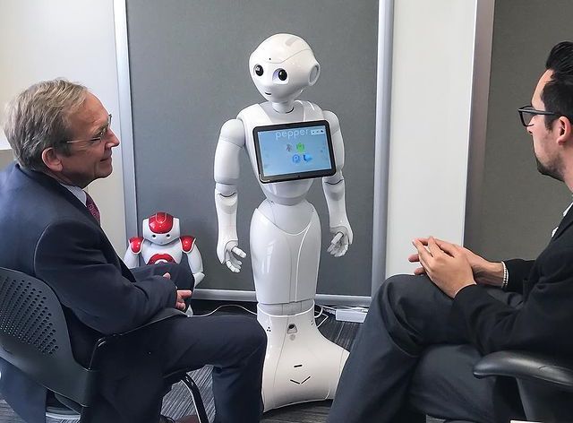 Two men in suits are viewing Pepper the robot.