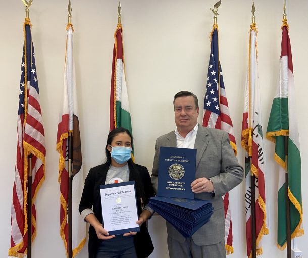 Woman and man holding certificates standing in front of flags indoors
